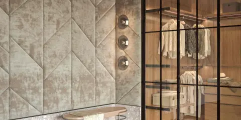 Ingresso con boiserie moderne in tessuto trapuntato geometrico, panca in legno e vimini, e cabina armadio a vista con illuminazione integrata.