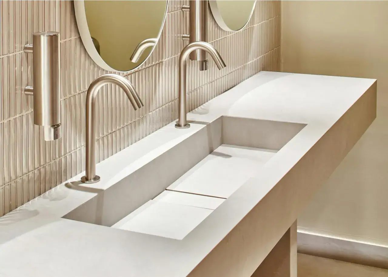 Lavabo integrato in Dekton o gres, con rubinetti a cascata e specchi rotondi.