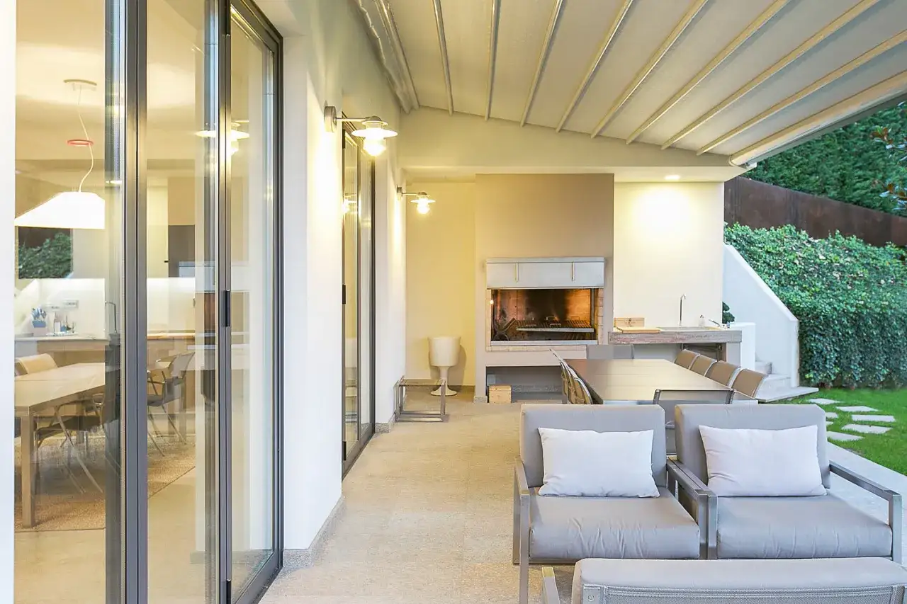 Veranda aperta con camino, tavolo da pranzo e comode poltrone. Idee per arredare una veranda aperta con stile e funzionalità.