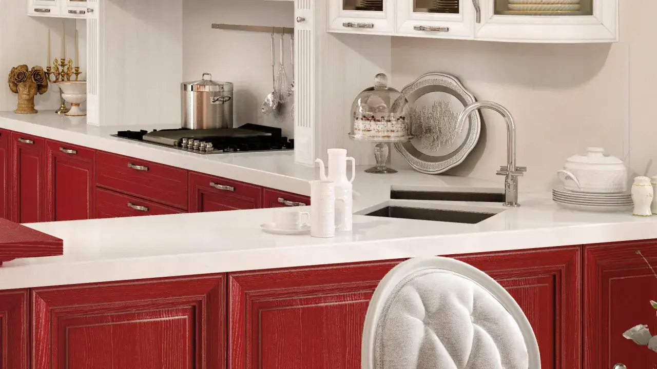 Cucina con ante rosse, piano bianco, pentola sul fornello, torta sotto campana di vetro. Okite cos'&egrave;? Un piano di lavoro resistente e bello.