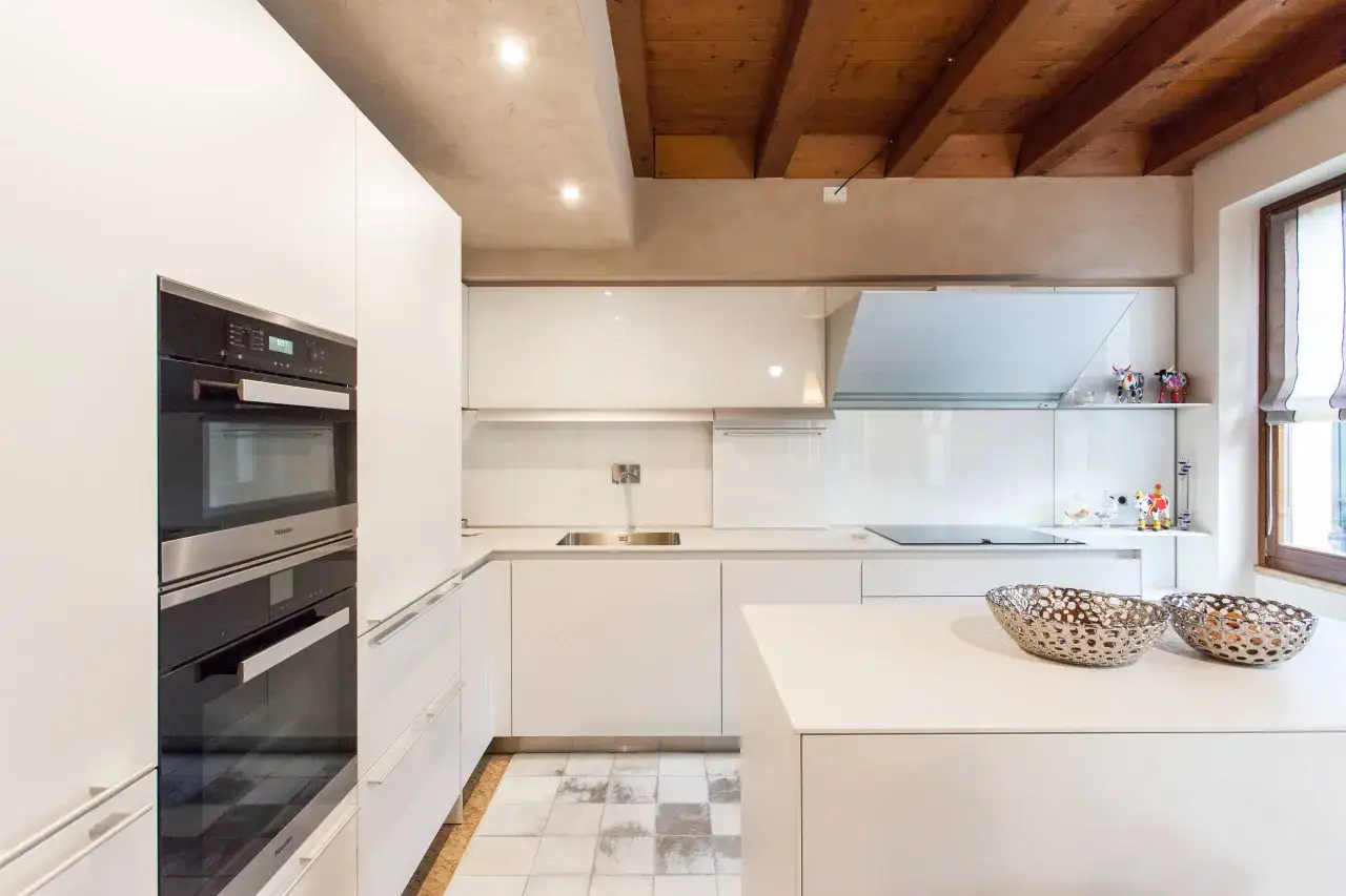 Cucina moderna con elettrodomestici a scomparsa e soffitto a travi a vista. L'altezza minima soffitto è valorizzata da faretti incassati.