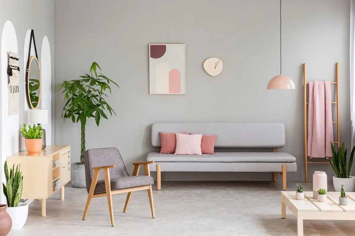 Un accogliente soggiorno con divano grigio, poltrona, tavolino e decorazioni in rosa pastello, come la coperta appesa alla scala di legno.