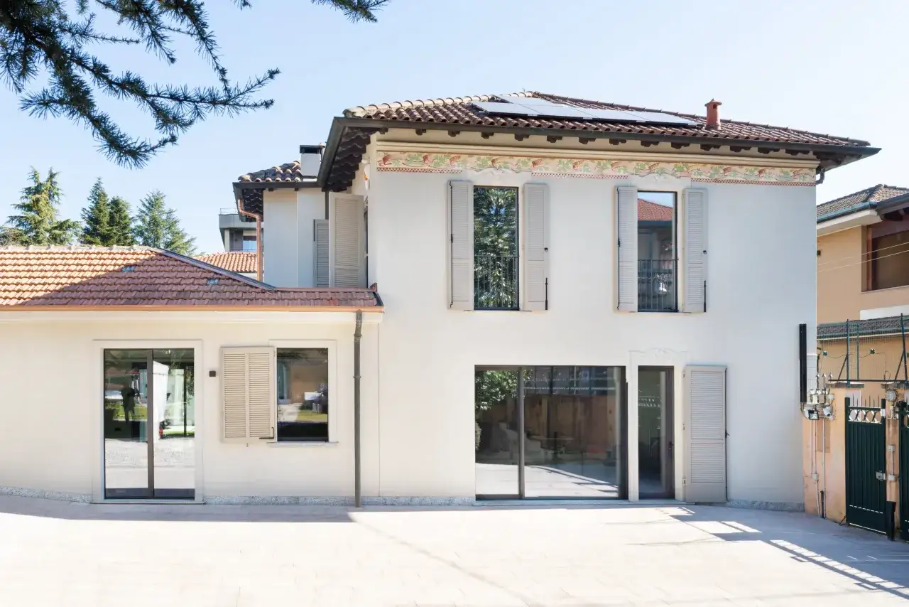 L'abbinamento colori facciata e serramenti crea un'armonia moderna. La casa bianca con dettagli decorativi si fonde con le persiane e gli infissi color sabbia.