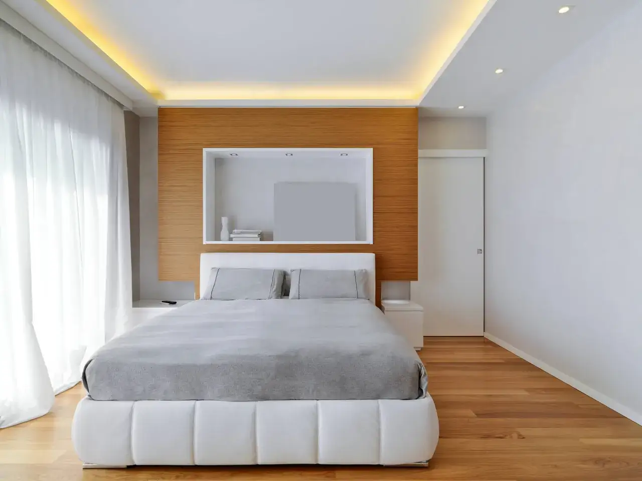 Illuminazione a scomparsa nel controsoffitto, un'idea moderna per il soffitto che crea atmosfera. Camera da letto minimalista con letto bianco e testiera in legno.